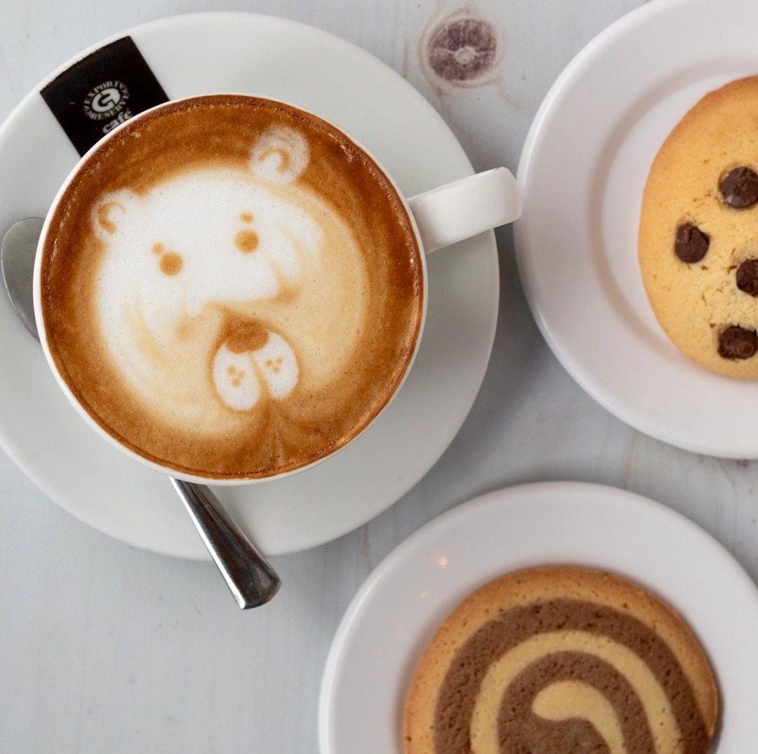 Café con leche con un osito dibujado en la espuma, junto a dos galletas