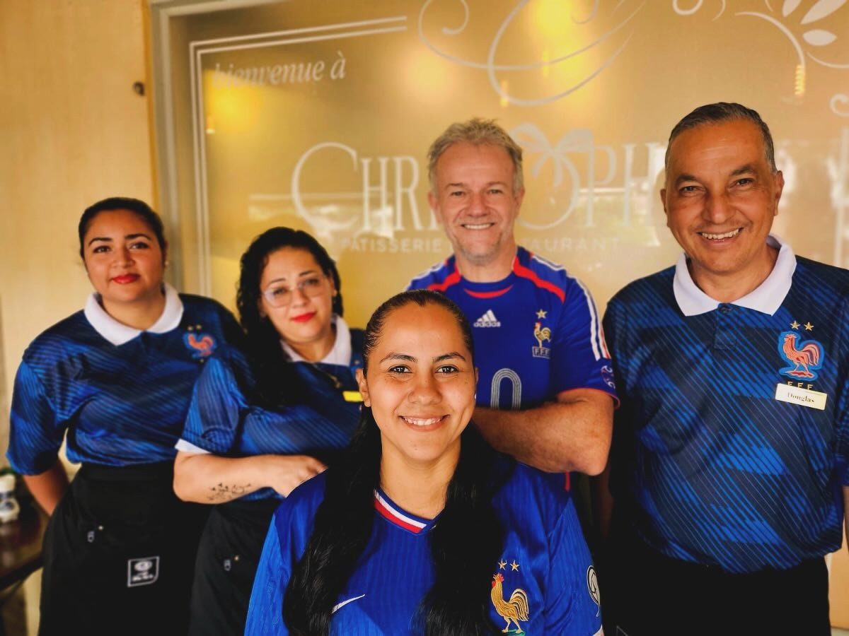 Cinco integrantes del equipo del restaurante sonriendo frente a la puerta de vidrio grabado