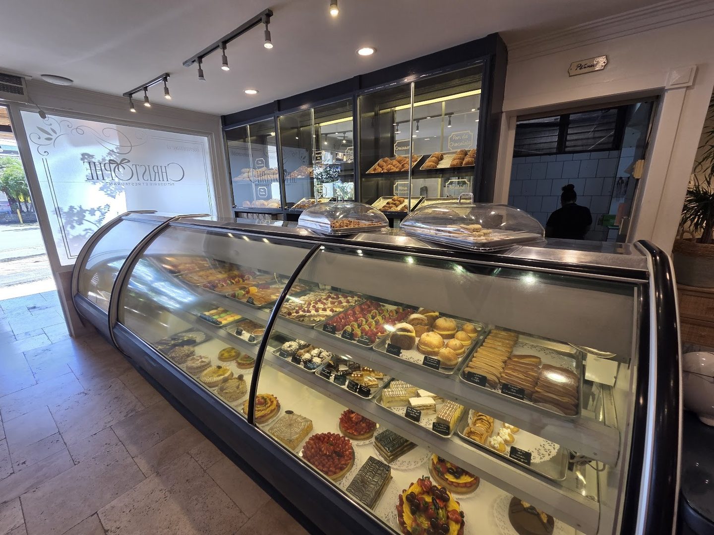 La vitrina de pasteles del restaurante, llena de tartas y éclairs, con el nombre Christophe grabado en el vidrio del fondo