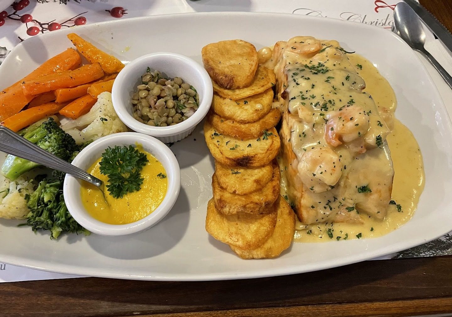 Plato de salmón con salsa de camarón, papas doradas y vegetales sobre el mantel individual de la casa