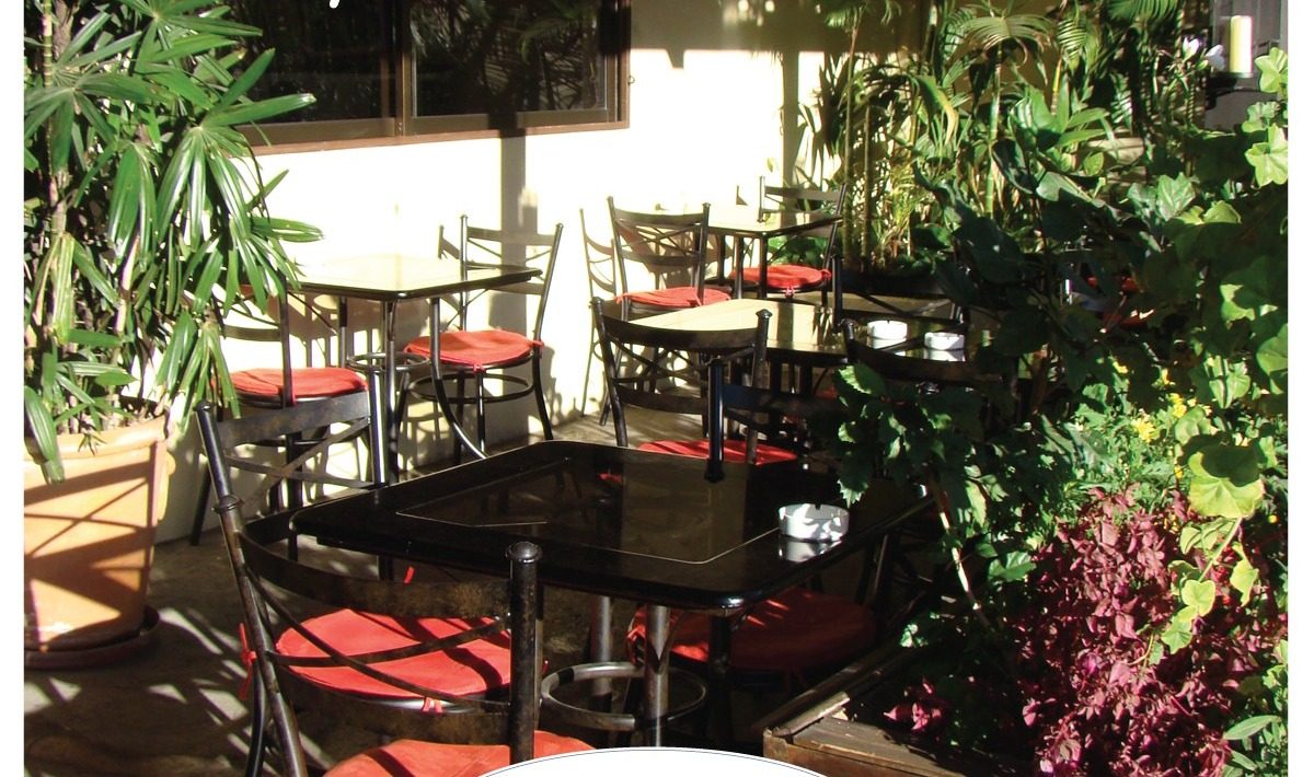 La terraza del restaurante con mesas de bistró negras y cojines rojos entre plantas